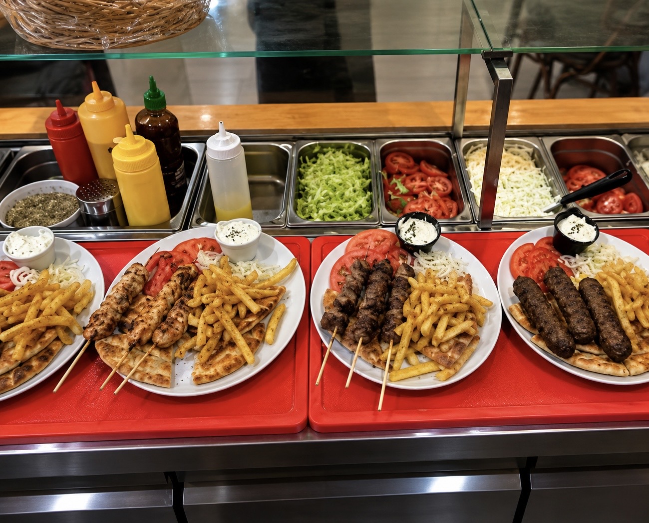 Four Greek souvlaki plates with chicken, pork and kebab skewers, pita, fries and toppings